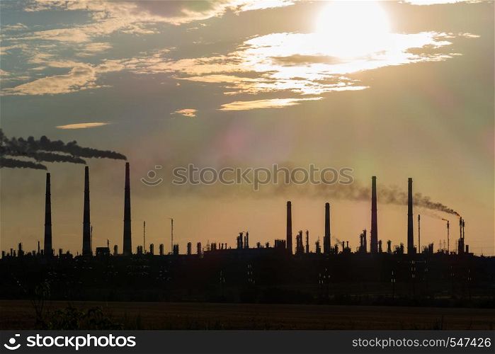 The silhouette of a Huge gas and oil processing plant with burning torches, pipes and distillation of the complex.. The silhouette of a huge gas and oil processing plant with burning torches, pipes and distillation of the complex