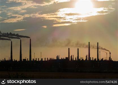 The silhouette of a Huge gas and oil processing plant with burning torches, pipes and distillation of the complex.. The silhouette of a huge gas and oil processing plant with burning torches, pipes and distillation of the complex