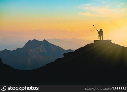 The silhouette of a lover taking a selfie on a mountain top During sunset time