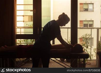 The silhouette of a masseuse as she is treating a client on a massage table