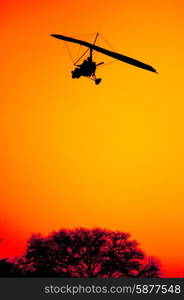 The silhouette of an ultra light aircraft on final approach as it comes in for landing against the red orange sky of a beautiful sunset at Victoria Falls in Zambia.