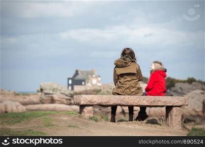 the sisters are sitting on a bench near the sea and the shore at the Tregastel, Brittany. France