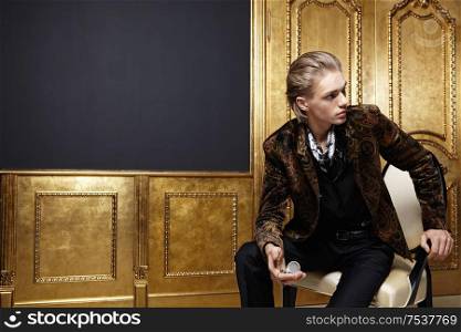 The sitting young man with watch against a gold door