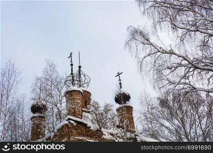 The skeletons of the domes of the old dilapidated church, covered with snow against the gray sky on a winter day.