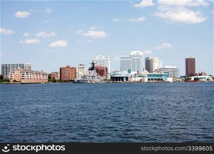 The skyline of Norfolk, Virginia on a nice summer day seen from Craford Bay. Tall buildings and Nauticus marine terminal and museum, and the US Navy battleship USS Wisconsin (BB-64) in it?s harbor port.