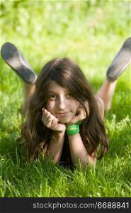 The smiling dark-haired girl-teenager lays on a green lawn in sunlight patches