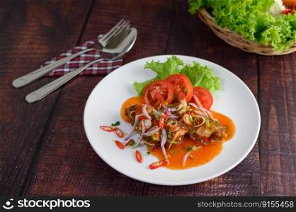 The spicy salad of canned sardines with tomato sauce mixed with herb in white dish and sparken stainless spoon and fork over napkin, cooking ingredient in weave basket on wooden table, copy space