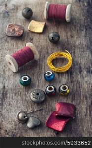 The spool of thread,beads and wire for needlework on wooden background.