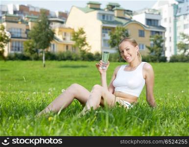 The sports girl drinks water sitting on a grass. Summer and sports