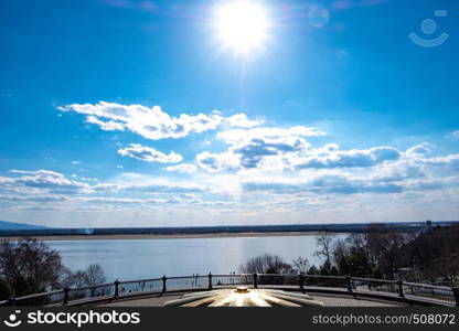 The spring Park is illuminated by the bright sun. View of a large and powerful river. On the bright blue sky beautiful white clouds.. View of the Amur river against the blue sky with white beautiful clouds. Bright spring sun. Russia, Khabarovsk.