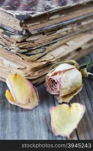 The stack of old books and dried rose lying on an old wooden board