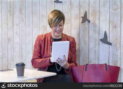 The strict business lady sits at a little table in cafe, uses the Internet on the tablet and has coffee.