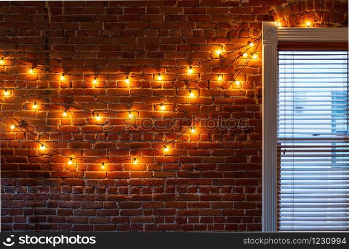The string of vintage lights bulbs inside at night, lights on a brick wall background, selective focus. Lights bulbs inside