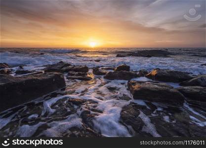 The stunning seascape with the colorful sky and water foam at the rocky coastline of the Black Sea