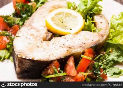 The sturgeon steak with salad and lemon on the plate. The sturgeon steak