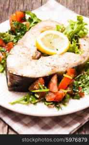 The sturgeon steak with salad and lemon on the plate. The sturgeon steak