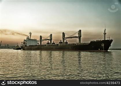 The stylized semi-antique photo. The ore carrier heaves out of the harbor on a tow, the photo is taken at sunset.