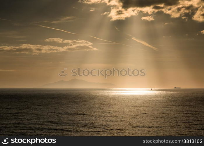 The sun beams down on a yacht and tanker with the sihouette of the isla of Elba in the distance