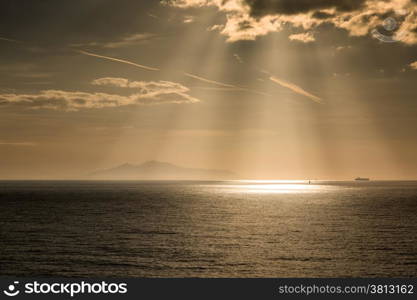 The sun beams down on a yacht and tanker with the sihouette of the isla of Elba in the distance
