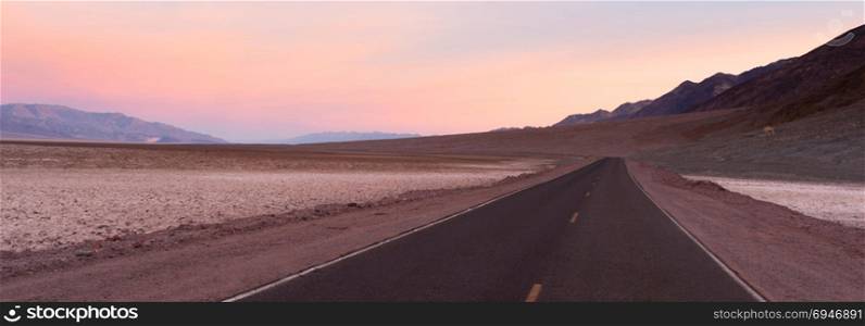 The sun creates pink hues in the sky as it rises in the desert of Death Valley National Park