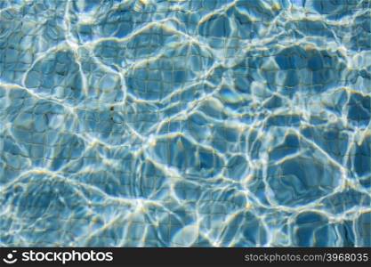 The Sun reflection on the blue clear water ripples of swimming pool with mosaic floor.