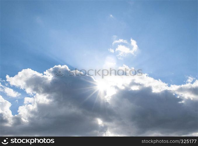 The sun?s rays come out from behind the clouds in the bright blue sky.