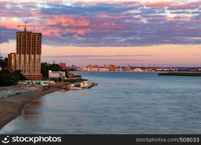 The sun sets over the Amur river. Buildings of the city of Khabarovsk in Golden pink. There are beautiful clouds in the sky.. Sunset over the city of Khabarovsk and the river Amur.