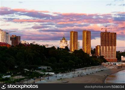 The sun sets over the Amur river. Buildings of the city of Khabarovsk in Golden pink. There are beautiful clouds in the sky.. Sunset over the city of Khabarovsk and the river Amur.