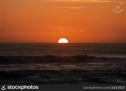 The sun slipping over the Atlantic Ocean at sunset near the Cape of Good Hope in South Africa. The circle of the sun is distorted by the air and clouds at the horizon.