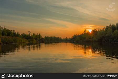 the sun slowly sets behind the treetops and a beautiful lake, which reflects the forest and sunset on a quiet summer evening. lake at sunset