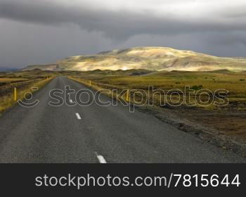 The sunlit Rhyolite Mountains of Myrdalur, Iceland, on a grim, overcast day, with the Number one ring road leading towards the volcanic mountain ridge