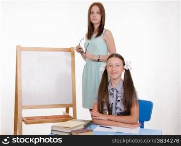 The teacher stands at the blackboard, a student sitting at a desk and listening to the teacher
