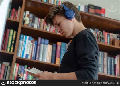 The teenage listens to music and reads book in front of library at home