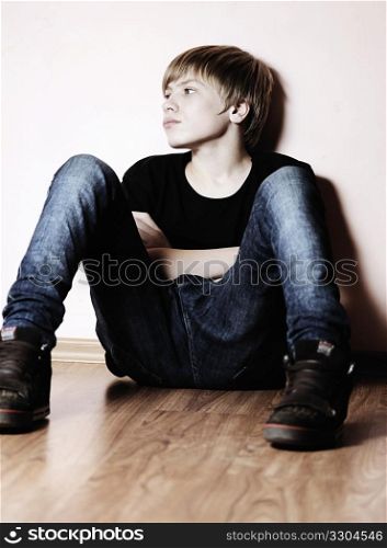 The teenager in a black vest sits about a wall