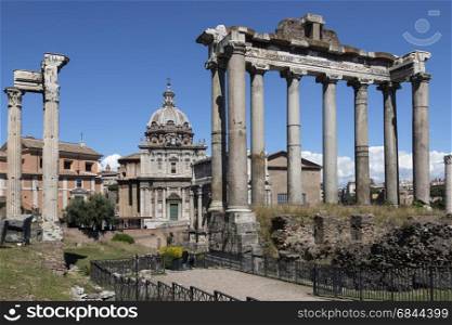The Temple of Saturn and (on left) the Temple of Vespasian and Titus in the Roman Forum in the city of Rome, Italy. Gradual collapse over the centuries has left nothing but the front portico standing. The ruins of the temple stand at the foot of the Capitoline Hill in the western end of the Forum Romanum. Nearby is the church of Santi Luca-e-Martina.. Temple of Saturn - Roman Forum - Rome - Italy