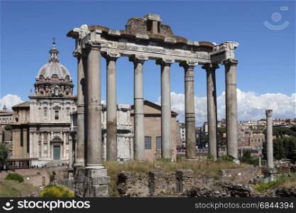 The Temple of Saturn in the Roman Forum in the city of Rome, Italy. Gradual collapse over the centuries has left nothing but the front portico standing. The ruins of the temple stand at the foot of the Capitoline Hill in the western end of the Forum Romanum. Nearby is the church of Santi Luca-e-Martina.. Temple of Saturn - Roman Forum - Rome - Italy