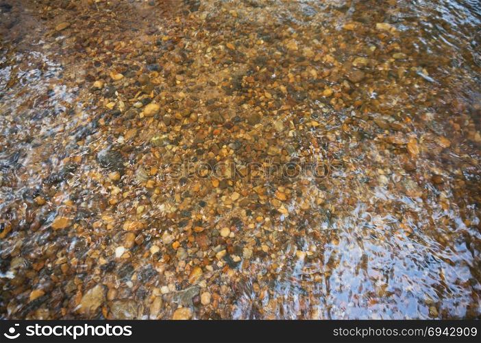 The texture of the bottom. The stones visible under the clear water. Water ripples of the river, the sun&rsquo;s rays on the rocks