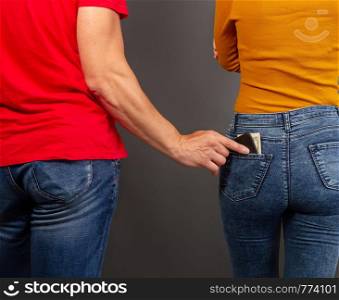 the thief, stepping up imperceptibly behind the girl, is trying to steal a purse with dollar bills from the back pocket of jeans. the thief steals the wallet