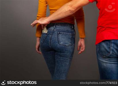 the thief, stepping up imperceptibly behind the girl, is trying to steal dollar bills from the back pocket of jeans. the thief steals dollars