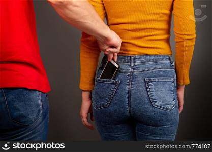 the thief stepping up imperceptibly behind the girl is trying to steal a smartphone from the back pocket of jeans. the thief steals the smartphone