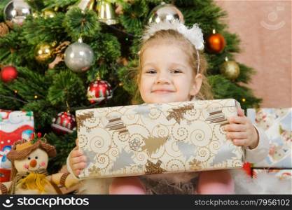 The three-year girl in a New Year&amp;#39;s dress sitting on a mat at the Christmas tree