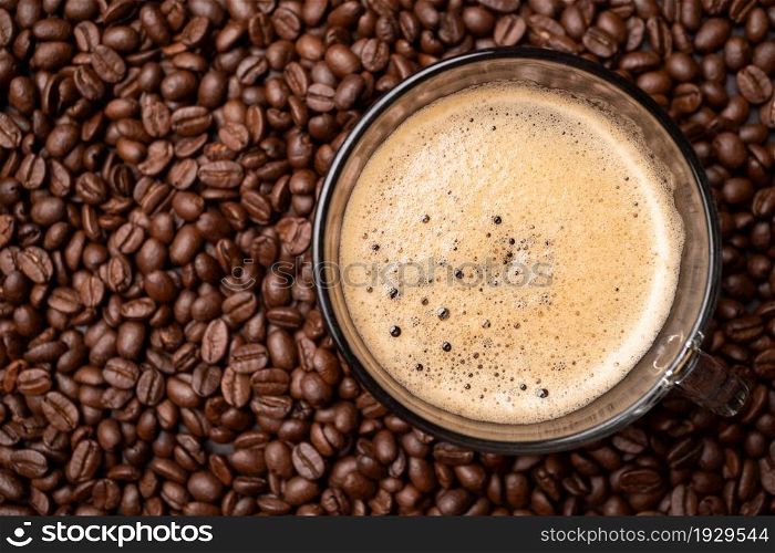 The top view of a coffee cup and group of black coffee beans is the background. Strong black espresso, Grounds of coffee background, texture