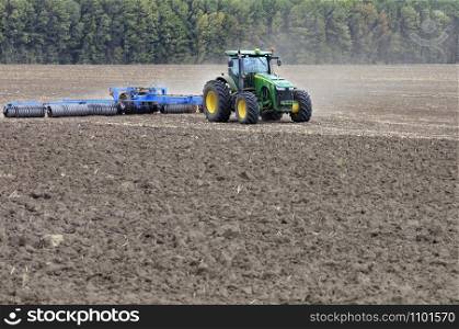 The tractor in the field shallow plow the soil with metal discs after the harvest.. Tractor in the field cultivates the soil after the harvest.