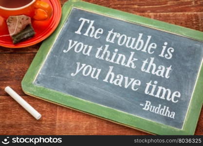 The trouble is you think that you have time- inspirational quote by Buddha on a slate blackboard with chalk and cup of tea