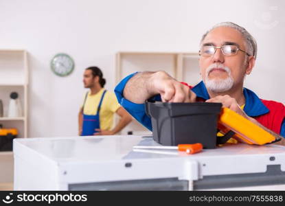 The two contractors repairing fridge at workshop. Two contractors repairing fridge at workshop