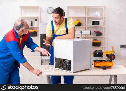 The two contractors repairing fridge at workshop. Two contractors repairing fridge at workshop