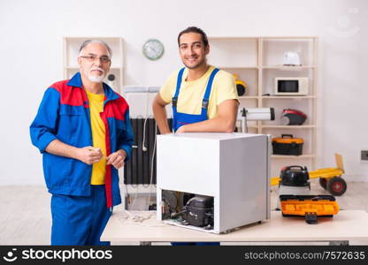 The two contractors repairing fridge at workshop. Two contractors repairing fridge at workshop