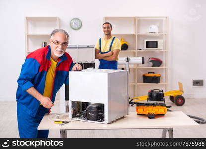 The two contractors repairing fridge at workshop. Two contractors repairing fridge at workshop