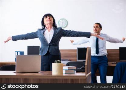 The two employees doing sport exercises in the office . Two employees doing sport exercises in the office
