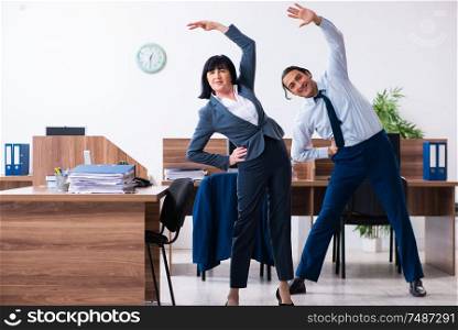 The two employees doing sport exercises in the office . Two employees doing sport exercises in the office